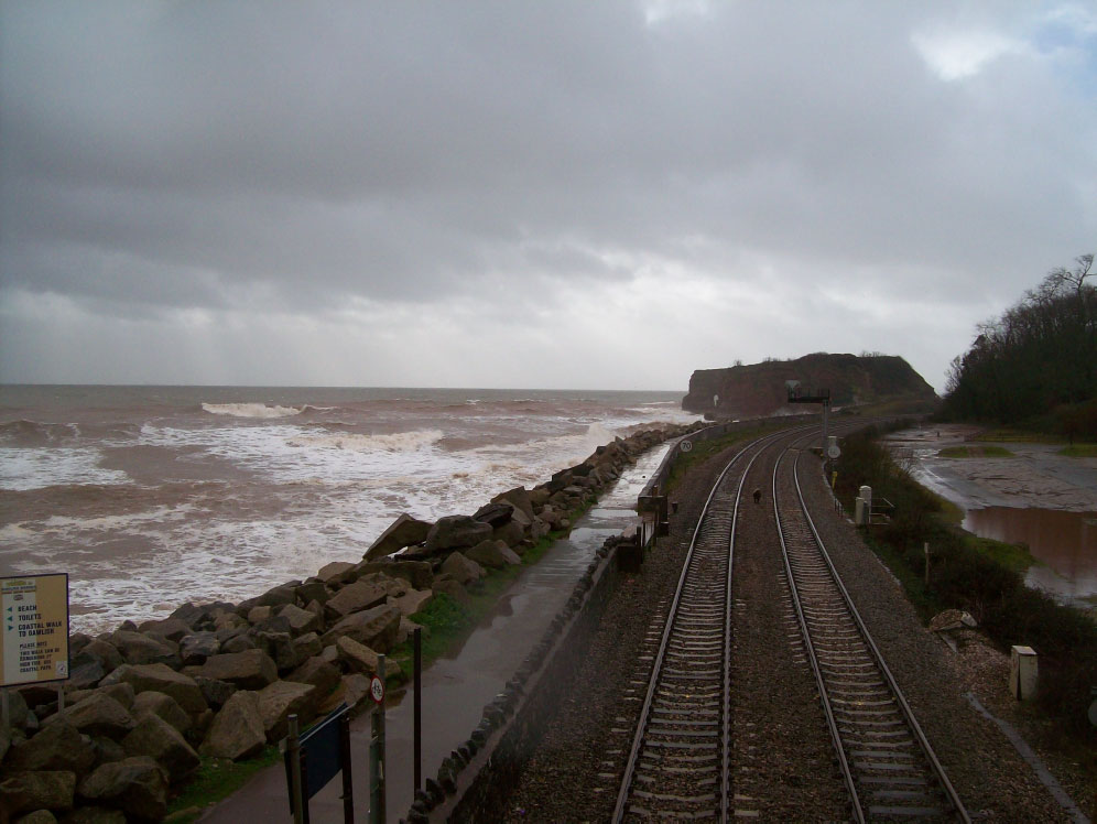 Langstone Rock is seen from the footbridge at Dawlish Warren. Waves were breaking over the rock armour now and again and there was a chance that the photographer would not have been drenched on his return; but he was. A siding extended along the walkway until 1941 to allow wagons laden with rock to be emptied where it was needed. The face of the original sea wall is now hidden behind the armour.