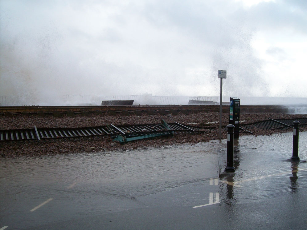 After the tide had turned, Marine Parade in Dawlish, was still being showered by waves. The ballast on the seaward side had already been resin bonded; the whole of the track after this was treated in the same way. Not apparent in these shots is the large number of spectators who had come out to see the destruction.